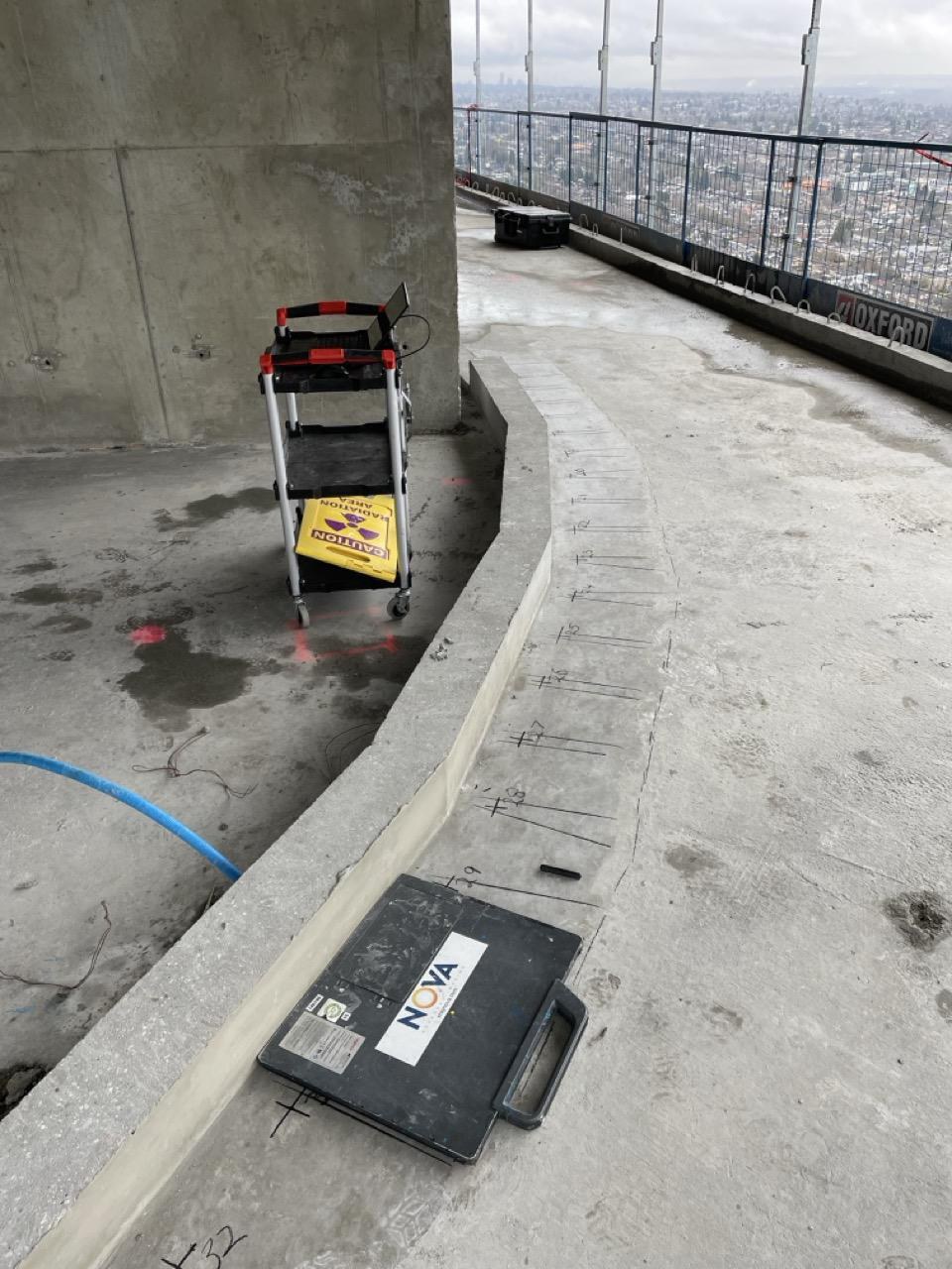 Digital concrete X-Ray on an active high-rise floor in Vancouver — the Nova detector panel positioned on the slab with coring locations marked, city skyline visible beyond the open edge